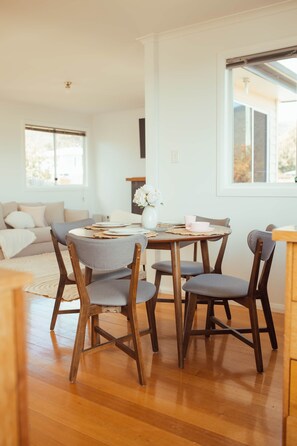 A dining area with a round table, six chairs, and a vase with flowers. - Modern 3BR Claremont Home | Parking & WiFi (Claremont)