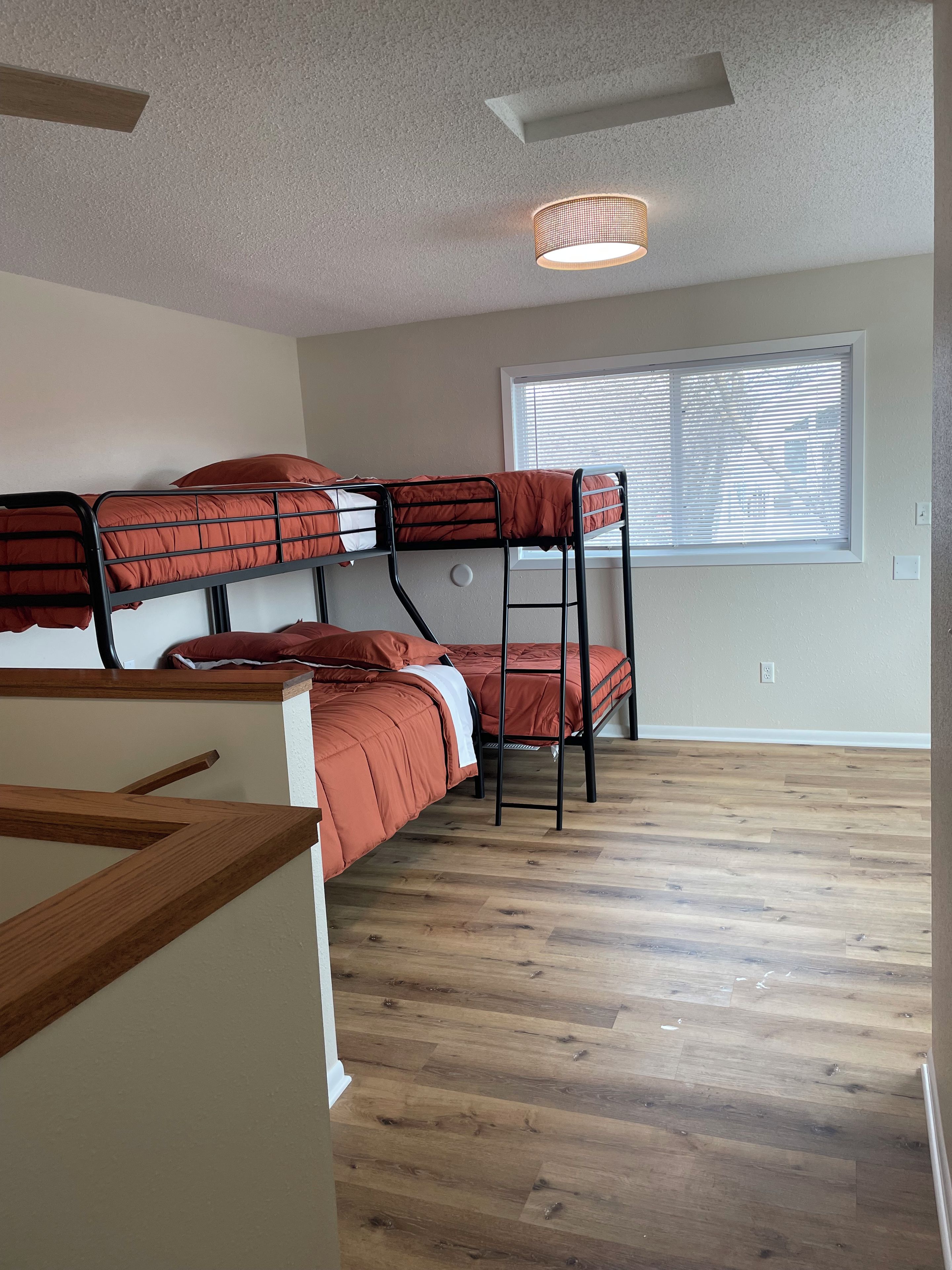 A bunk bed room with a window, wooden flooring, and a ceiling light fixture.