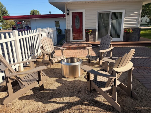 En patio med Adirondack-stole, pejse og et hvidt stakitéhegn.