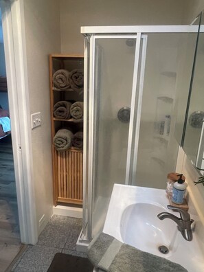 A bathroom with a glass-enclosed shower, a sink with a faucet, and a shelf with rolled towels. - Marina House - Lake Life and Shirley's Treats Next Door (Starbuck)