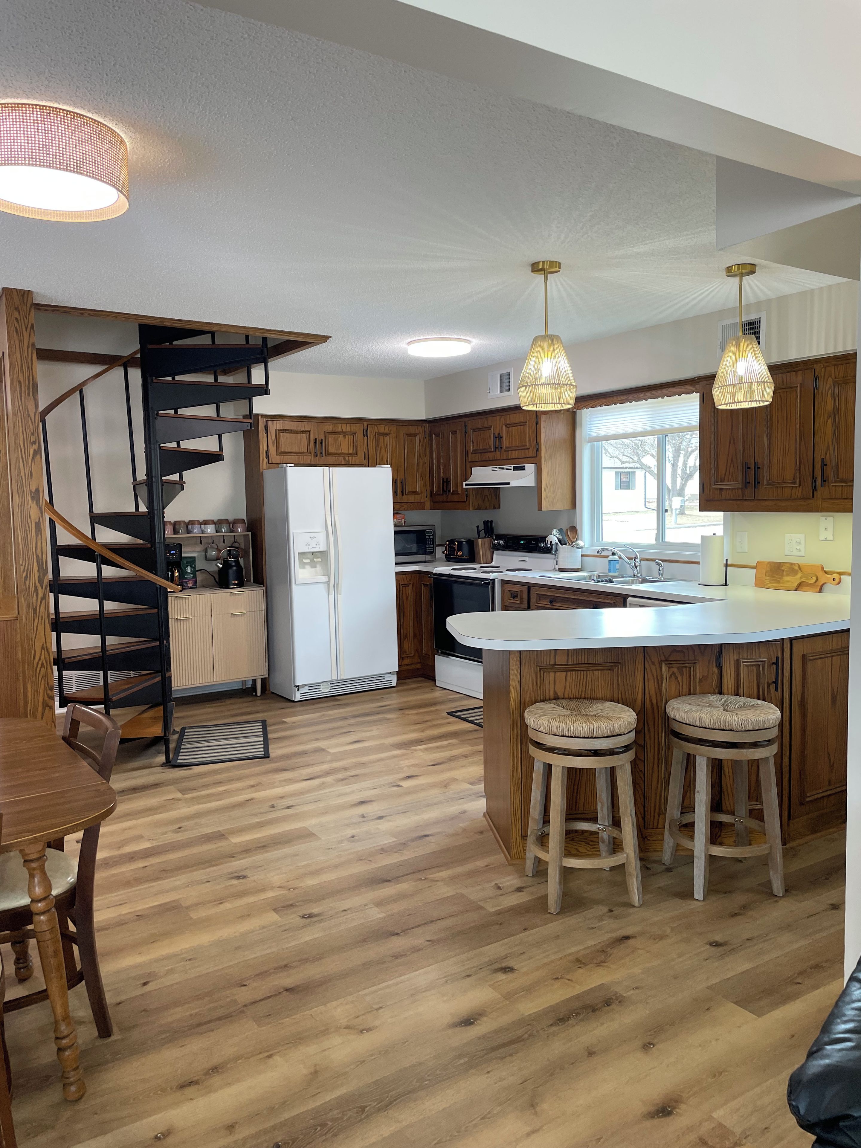Een moderne keuken met houten kasten, een centraal eiland met krukken, een ingebouwde spiltrap en hanglampen.