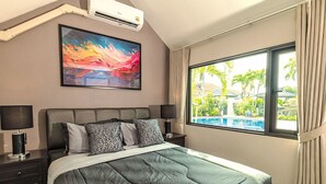 Een hotelkamer met een bed, twee nachtkastjes met lampen, een groot raam met gordijnen, een airconditioningsunit en een kleurrijk abstract schilderij aan de muur.