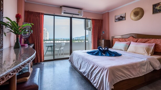 Une chambre d’hôtel avec un lit, un bureau, une chaise, une plante en pot et une vue sur la ville grâce à de grandes fenêtres.