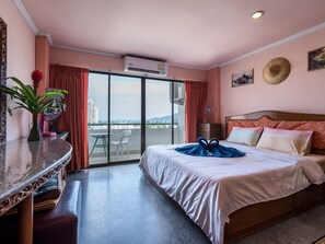 A hotel room with a bed, a desk, a chair, a potted plant, and a view of the city through large windows. - Condopatong Studio by Interhome (Phuket)