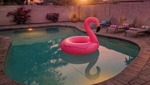Een zwembad met een roze flamingo drijvend, ligbedden en potplanten.