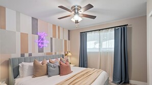 Een keurig opgemaakt slaapkamer met een bed, een plafondventilator, een nachtkastje en een raam met gordijnen.