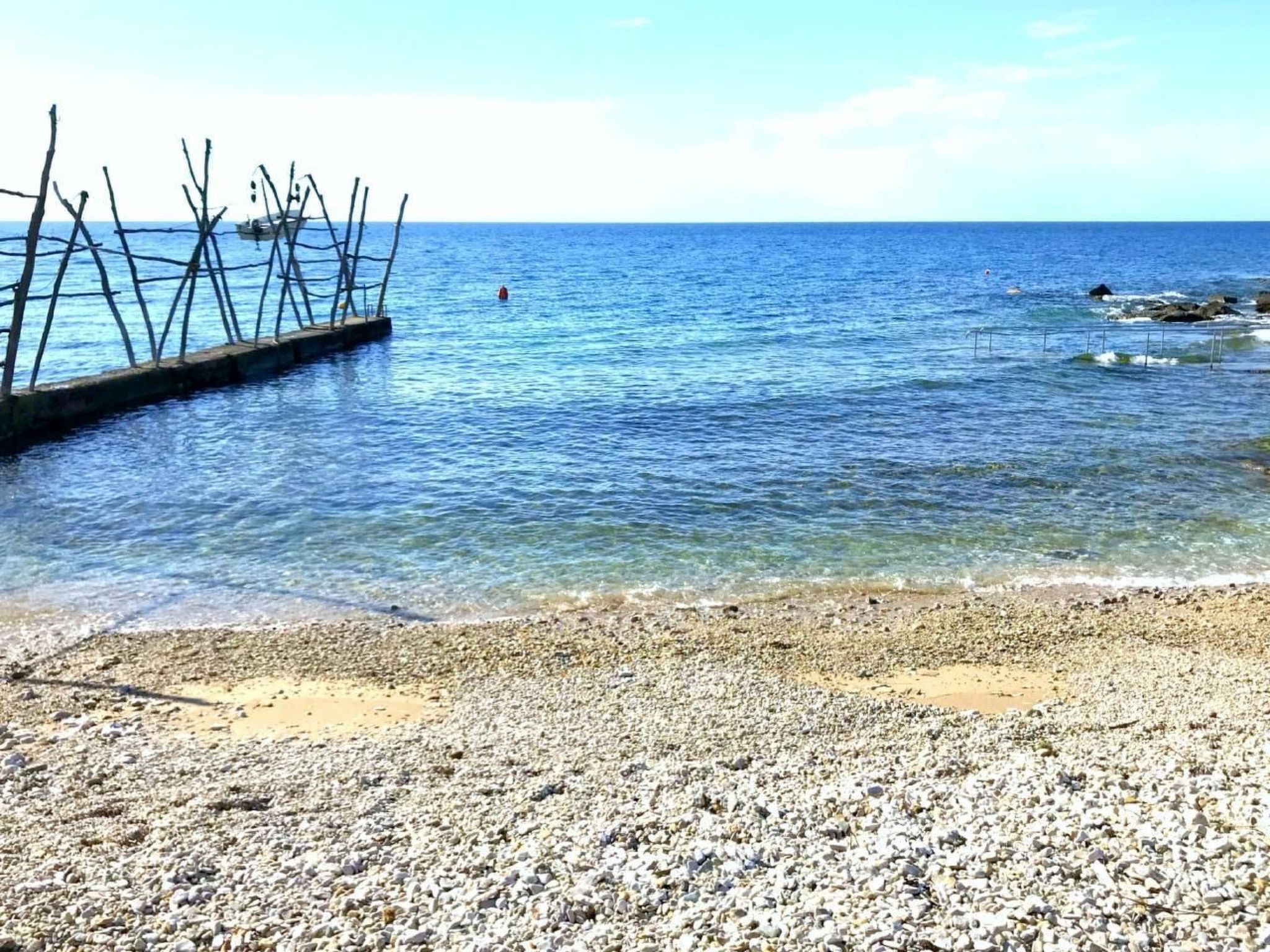 Una spiaggia di ciottoli con acque blu cristalline e una struttura in legno che si protende verso il mare.
