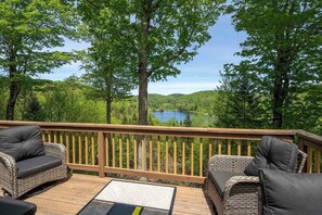 A deck with wicker furniture and a view of a lake surrounded by trees.