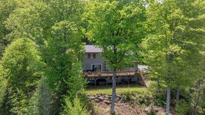 Ein Haus, umgeben von üppigen Grünflächen, mit einer Holzterrasse und einer Treppe, die zu einer zweiten Ebene führt.
