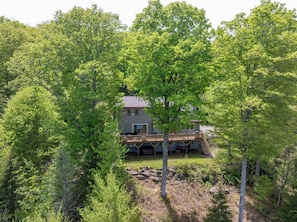 A house surrounded by dense green trees, with a wooden deck and a staircase leading to a second level.