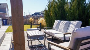 Un patio al aire libre con una mesa de madera, dos sillas blancas con cojines y un banco.