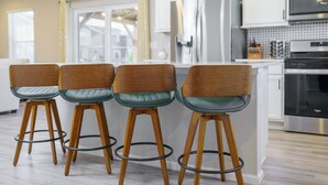 Una cocina moderna con armarios blancos, electrodomésticos de acero inoxidable y una zona de bar con taburetes de madera.
