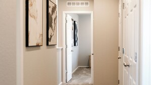 Un pasillo con paredes color beige, piso cubierto de alfombra y una puerta que da a otra habitación.