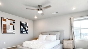 Un dormitorio amplio con una cama grande, un ventilador de techo y un ventanal con cortinas.
