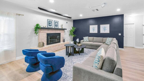 Een moderne woonkamer met een open haard, blauwe stoelen, een grijze bank en een donkerblauwe accentmuur.