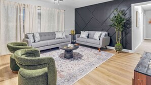 Een moderne woonkamer met een grijze zithoek, een salontafel en groene fauteuils.