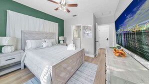 Een slaapkamer met een bed, nachtkastjes, een plafondventilator, een schilderij en uitzicht op een stadsbeeld.