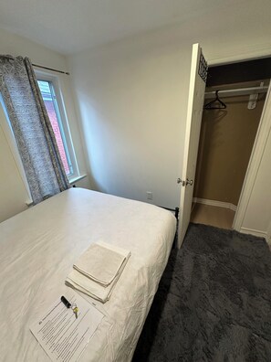 Ein Schlafzimmer mit einem Bett, einem fensterbelaubten Fenster, einer Tür zu einem Kleiderschrank und einem Teppichboden.
