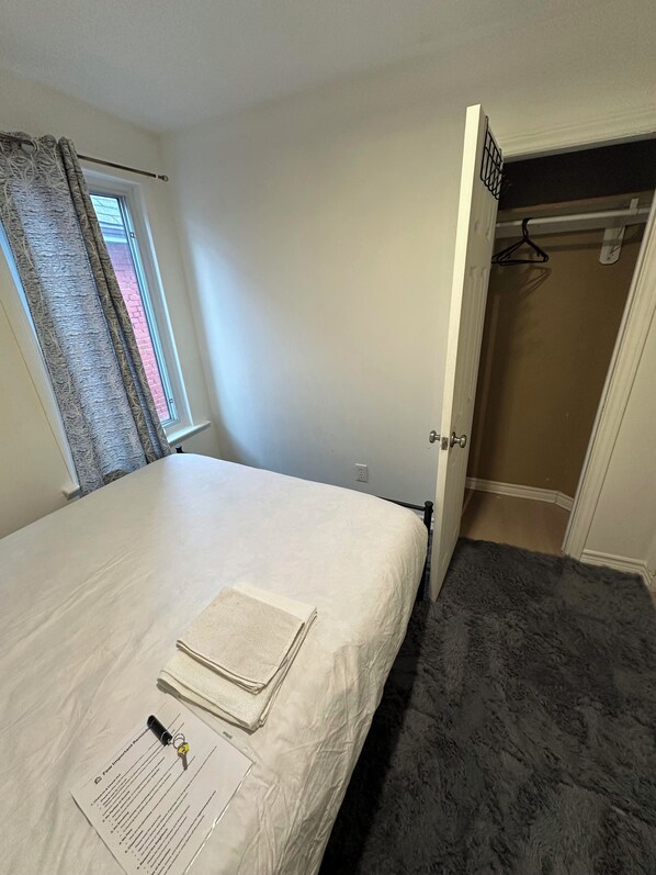 Une chambre  à coucher avec un lit, une fenêtre avec des rideaux, une porte donnant sur un placard et un sol recouvert de moquette.