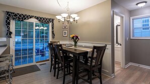 A dining area with a table and chairs, a chandelier, and a view through a glass door. - 3 Bedroom Homestead Getaway - Walkable Carrboro, Minutes to UNC (Carrboro)