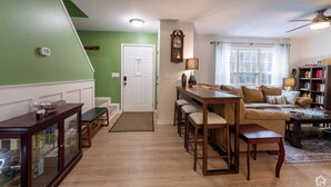 A living room with a sofa, coffee table, and bookshelf. There is a dining area with a table and chairs. The room has a green wall and a white door. - 3 Bedroom Homestead Getaway - Walkable Carrboro, Minutes to UNC (Carrboro)