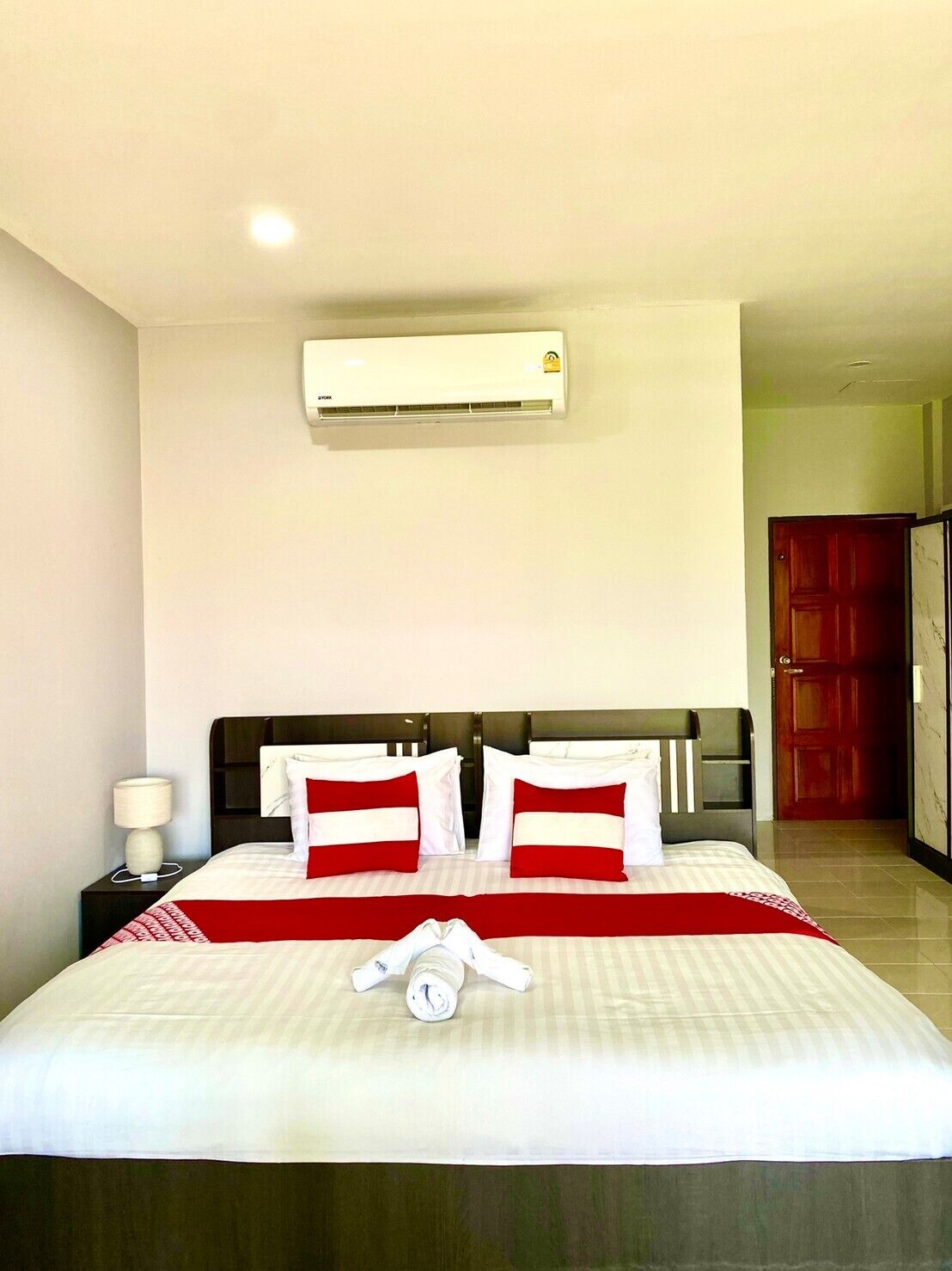Una habitación de hotel con una cama, una mesita de noche, aire acondicionado y una puerta.