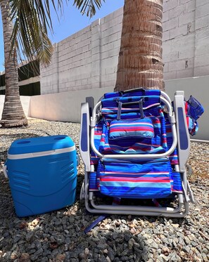 A beach chair with a striped cushion, a blue cooler, and a palm tree in the background. - Bright 2-Bedroom Fully Equipped House 7 mins Away to Palm Beach (Noord)