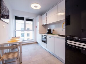 A modern kitchen with white cabinets, a black stove, and a window with blinds. - Luxuriöse Präsidentensuite by Interhome (Bucuresti)