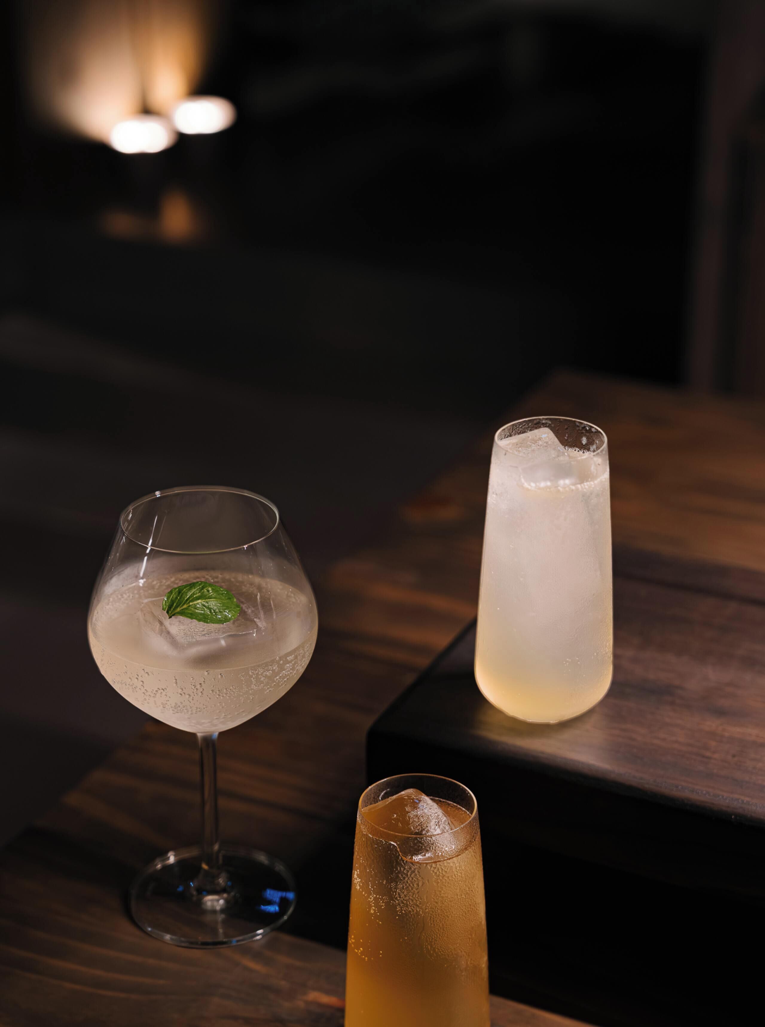 Three glasses of beverages on a wooden table with a dark background.
