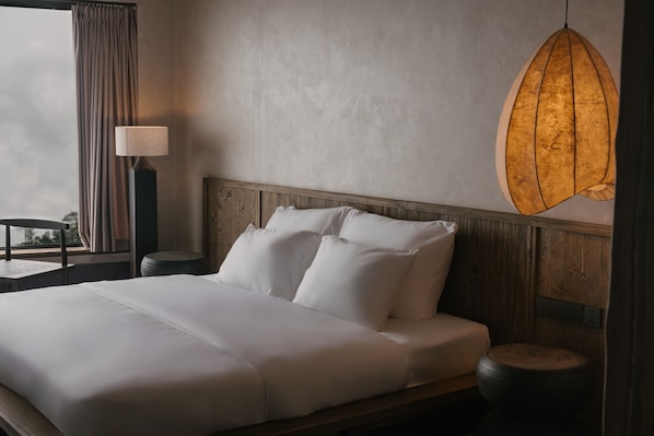 Una cama bien hecha con sábanas blancas, un cabecero de madera, una mesita redonda y una lámpara.