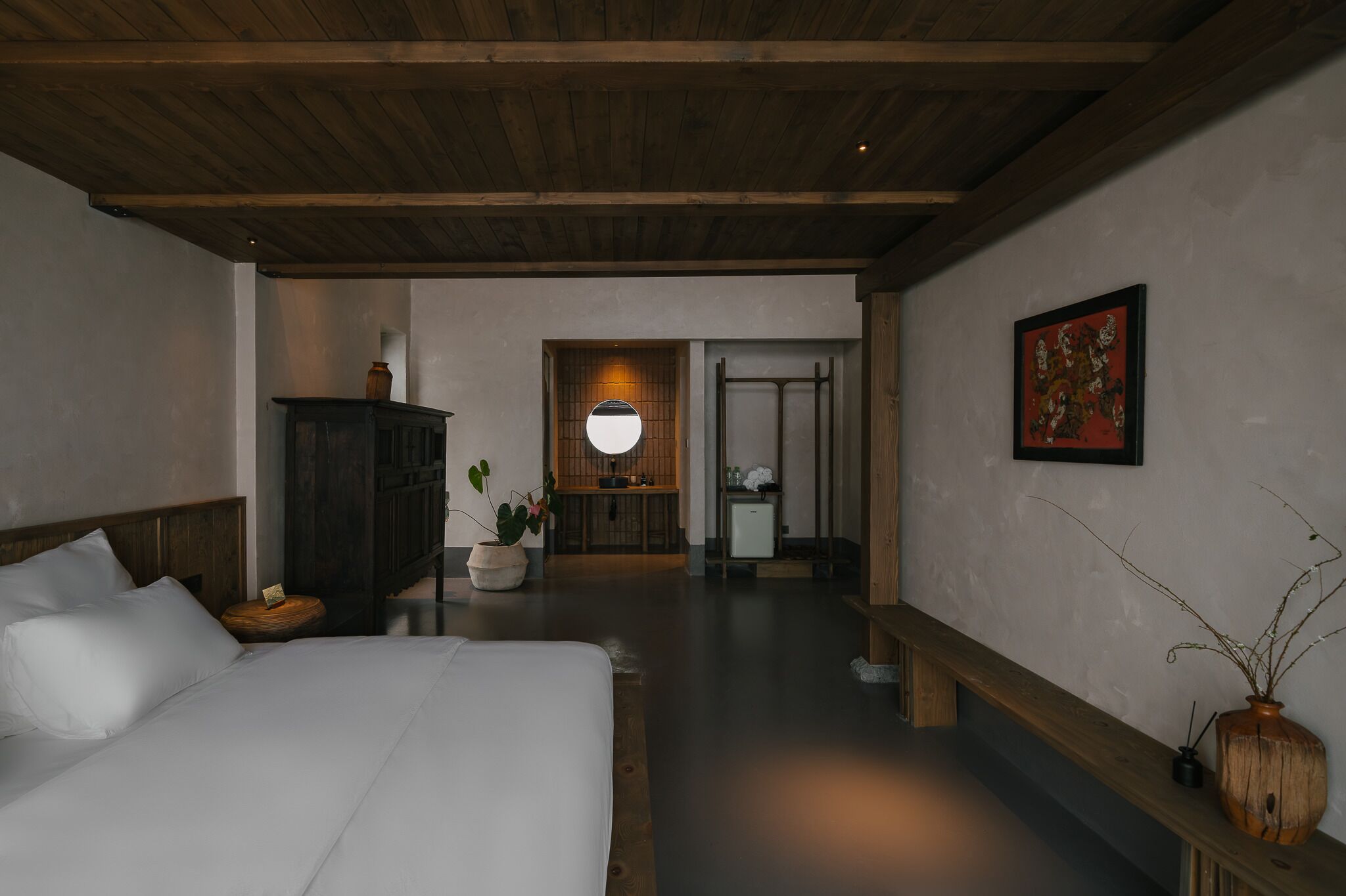 Un dormitorio con cama, mesita de noche y un tocador. Hay un cabecero de madera, un espejo y un mueble pequeño. Una planta en maceta está sobre la mesita de noche.