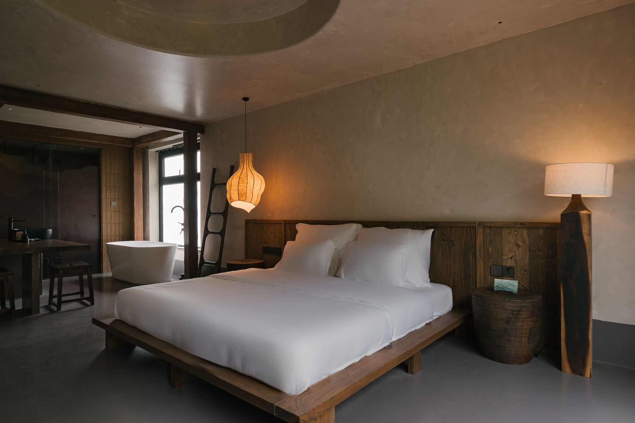 Un dormitorio moderno con una cama grande, un cabecero de madera, una lámpara de noche y una pequeña mesita redonda con una lámpara.