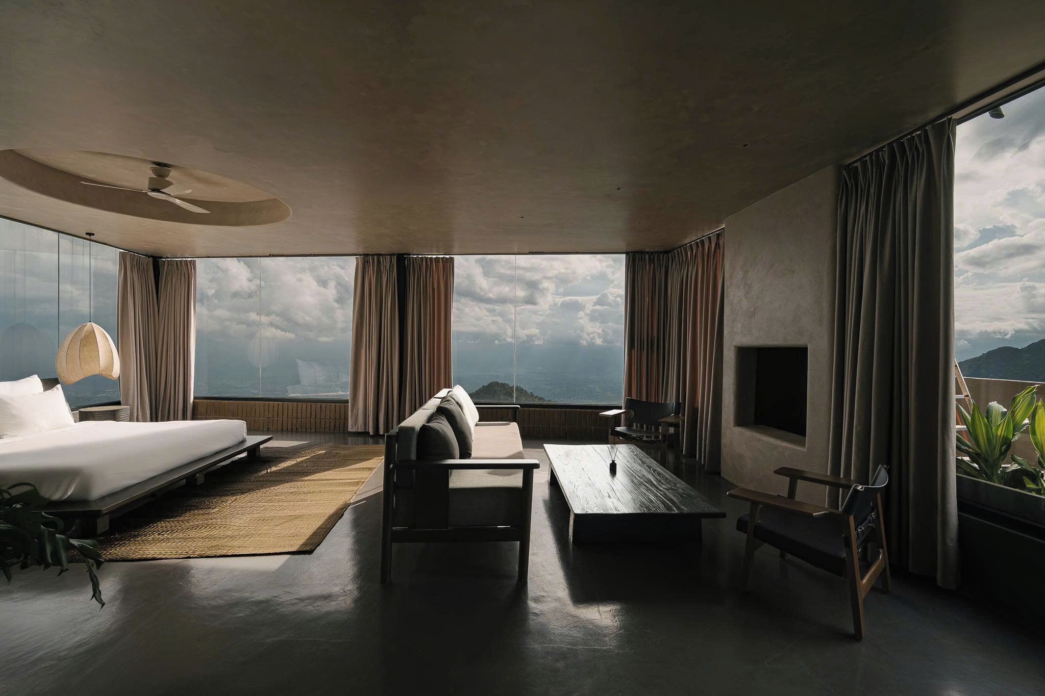 Ein modernes Hotelzimmer mit einem großen Bett, einer Couch, einem Couchtisch und einem Fernseher. Das Zimmer verfügt über große Fenster mit Blick auf das Meer und die Berge.