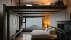 Un dormitorio con cama, mesita de noche, cómoda, ventana con cortinas y vista a la montaña.
