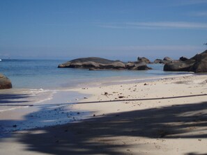 Una playa con rocas grandes, agua azul cristalina y una orilla arenosa.