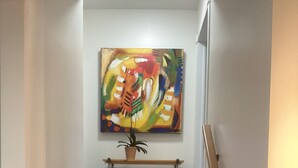 Un escalier avec des marches en bois, une rampe métallique et une peinture abstraite aux couleurs vives au-dessus d’une petite étagère sur laquelle se trouve une plante.