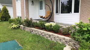 Une maison avec un mur de soutènement en pierre, une véranda avec une balançoire, et une variété de plantes et de fleurs.