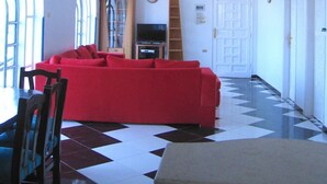 Ein geräumiges Wohnzimmer mit einem roten Sofa, einem Fernseher und einem Deckenventilator.