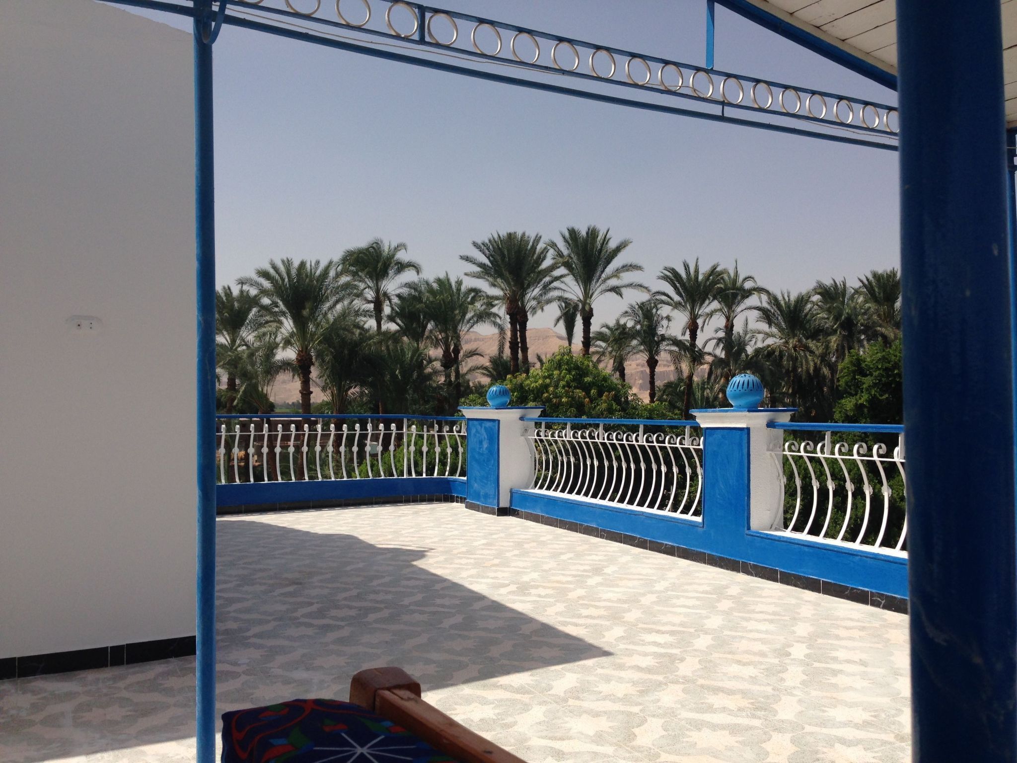 A covered outdoor area with a patterned floor, blue and white railings, and palm trees in the background.