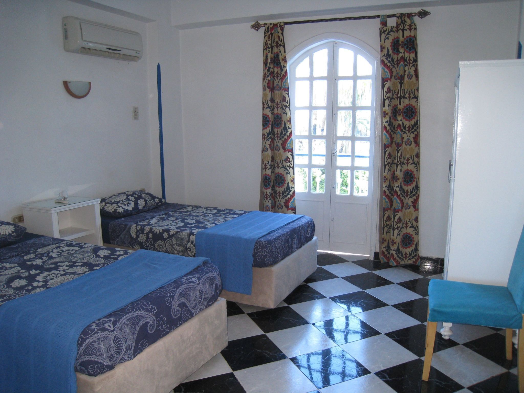 Une chambre avec deux lits, une chaise, une petite table et une porte avec des rideaux.