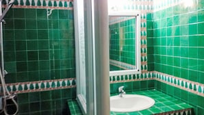 Ein Badezimmer mit grünen Fliesen, einem weißen Waschbecken und einer Duschkabine.