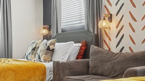 Una moderna camera d'albergo con un divano grigio, un letto con coperta gialla e una parete decorata.