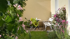 En hyggelig udendørs siddeplads med et bord og to stole, omgivet af frodigt grønt og blomstrende planter.