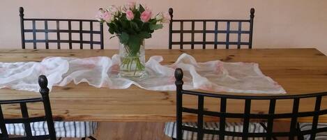 Una mesa de madera para comer con un centro de flores, rodeada por cuatro sillas con estructura de metal negro y cojines a rayas.