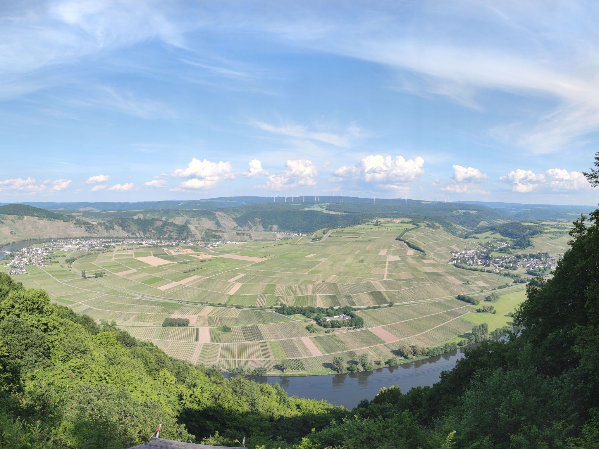 Et panorama over et dalområde med marker, en flod og vindmøller i det fjerne.