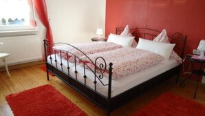 Ein Schlafzimmer mit einem Metallbettgestell, zwei Nachttischen, einem roten Teppich und einem Fenster mit roten Vorhängen.