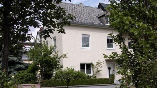Ein zweistöckiges Haus mit weißer Fassade, zahlreichen Fenstern und einem kleinen Vorgarten.