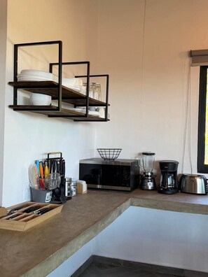 Una cocina con microondas, licuadora, cafetera y utensilios sobre la encimera.