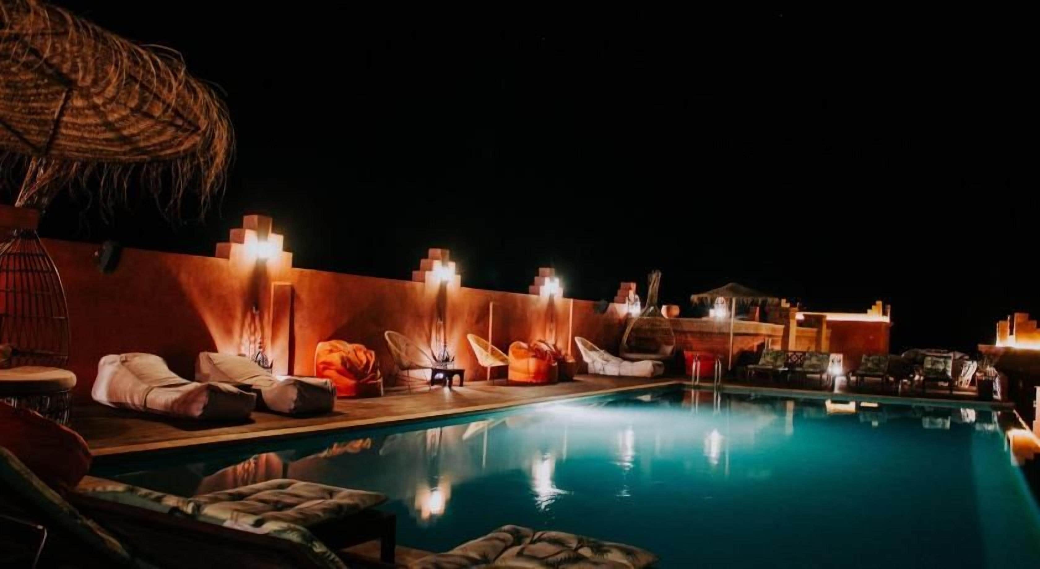 A nighttime pool area with lounge chairs and umbrellas, surrounded by walls with built-in lighting.
