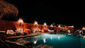 A nighttime pool area with lounge chairs and umbrellas, surrounded by walls with built-in lighting.